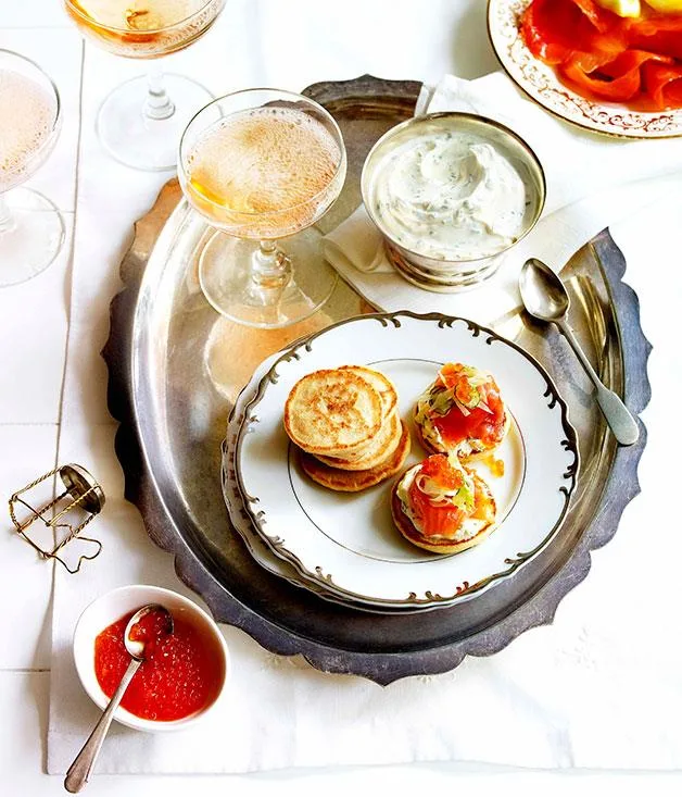 Plate of blini with smoked salmon, cream sauce, and caviar on a tray with champagne flutes.