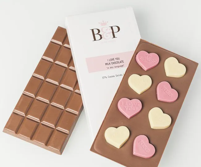 Chocolate bar with heart-shaped candies inscribed with romantic phrases like "I Love You," on a white background.