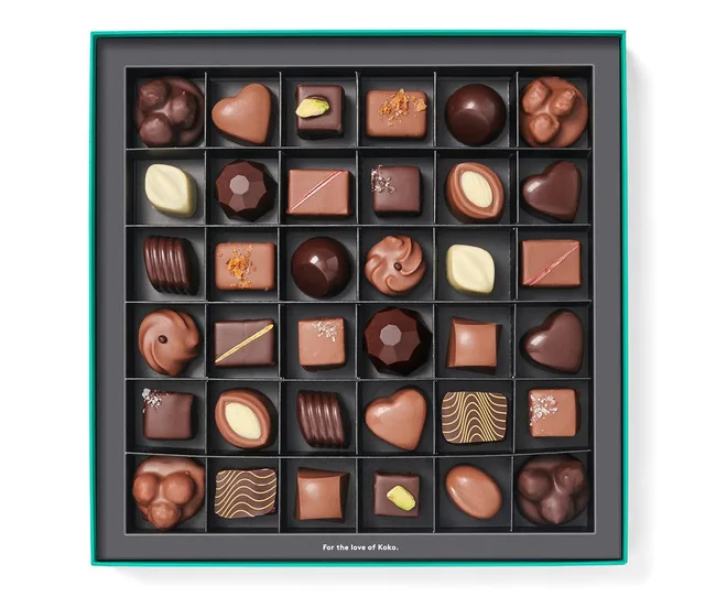 Assorted chocolates in a grid box, including heart shapes and chocolates with nuts, in a teal-bordered package.