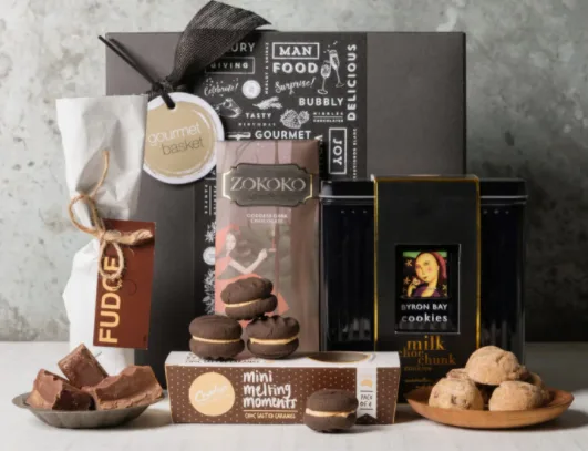 Gift basket with fudge, cookies, and chocolates arranged in front of a black "Gourmet" box.