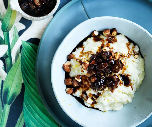 Creamy rice pudding topped with chopped nuts and a dark syrup in a white bowl on a blue plate.