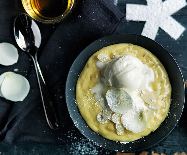 Creamy dessert topped with white ice cream, garnished with sliced almonds and powdered sugar, served in a dark bowl.