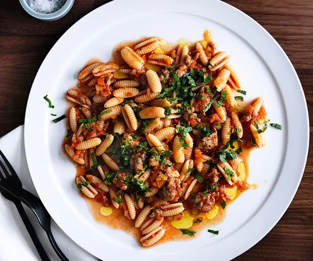 Plate of gnocchi with sausage ragu and fresh herbs on a table setting.