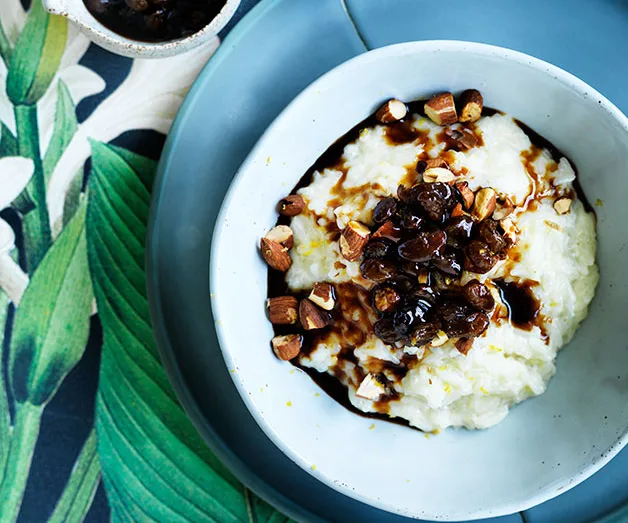 A bowl of rice pudding topped with nuts and a dark sauce on a blue plate, on floral-patterned fabric.