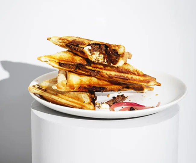 Grilled sandwiches stacked on a white plate with filling visible.