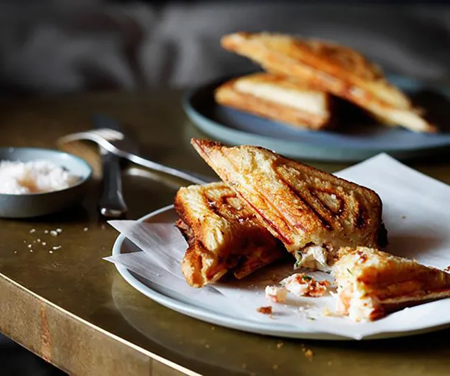 Grilled cheese sandwich cut into triangles on a white plate with a side of salt in a small dish.