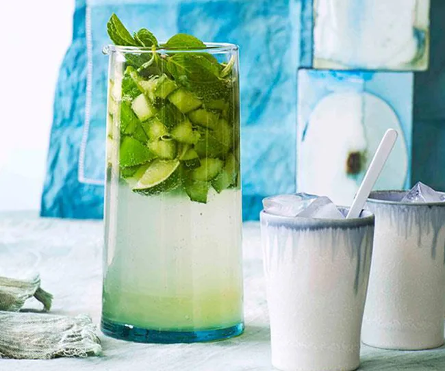 Refreshing cucumber mojito in a tall glass with mint, next to two cups with ice.