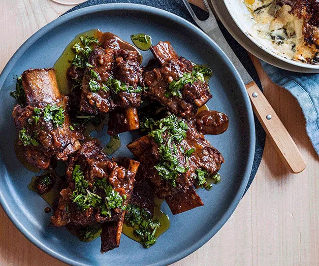 Braised short ribs garnished with herbs served on a blue plate.
