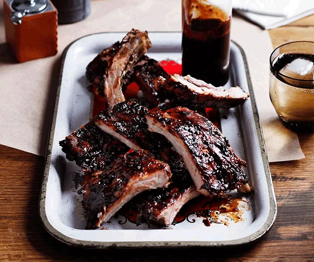 Barbecue ribs with sauce on a tray, accompanied by a drink with ice on the side.