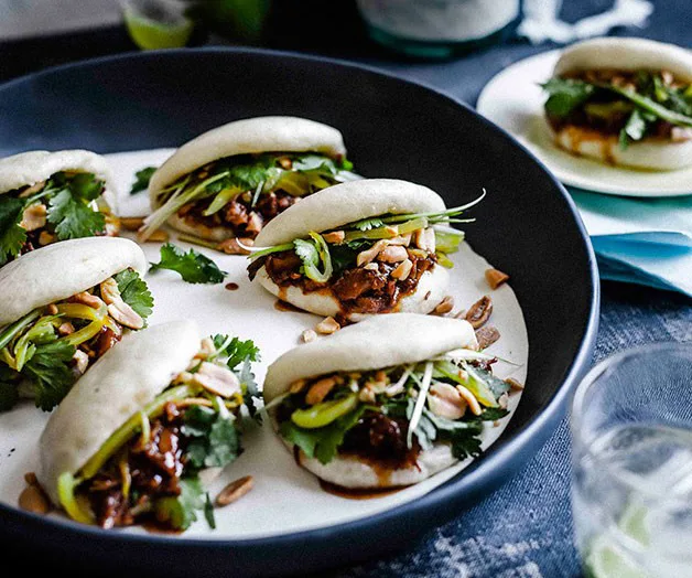 Bao buns filled with meat, cilantro, and vegetables on a dark serving platter.