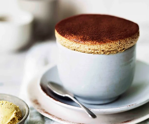 Coffee soufflé in a white cup on a saucer with a spoon, served with a scoop of ice cream.