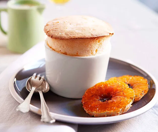 Creamy souffle in a white ramekin with caramelized pineapple rings on a plate, accompanied by two spoons.