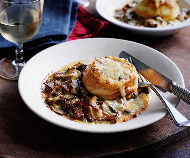 Plate of mushroom ragout with cheese soufflé, served with a knife and fork, and a glass of white wine on the side.