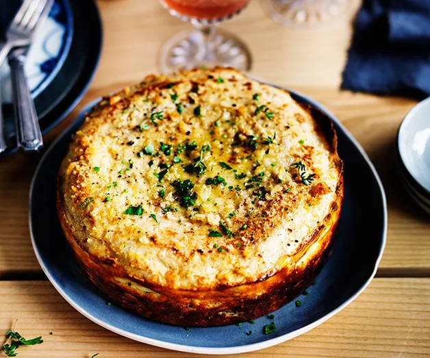 Savory potato and pork pie garnished with herbs on a wooden table.