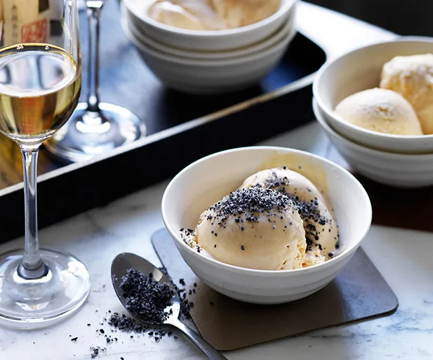 Vanilla ice cream with poppy seeds in a bowl, next to a glass of wine on a table.