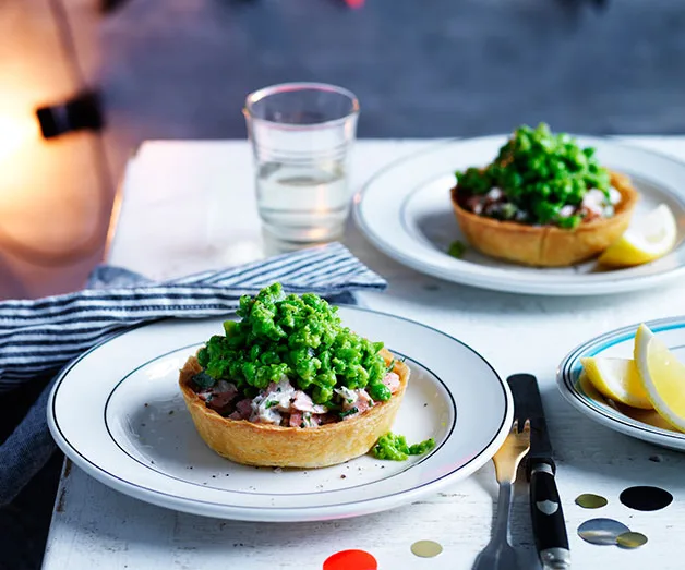 Plate of pie topped with mashed peas, served on a table with lemon wedges, a glass of water, and cutlery.