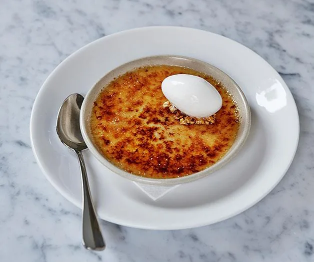 Cr&egrave;me br&ucirc;l&eacute;e with caramelized top and a scoop of ice cream on a white plate with a spoon beside it.