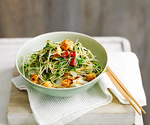 Bowl of prawn and sprout salad with herbs and red chili on a white napkin, wooden chopsticks on the side.