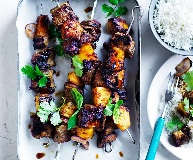 Grilled lamb and pineapple skewers with herbs, served beside a bowl of rice.