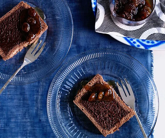 Two slices of chocolate cake with fig compote on glass plates, placed on a blue textured fabric.