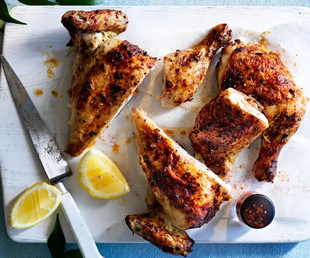 Grilled chicken pieces on a white cutting board with lemon wedges and spices.