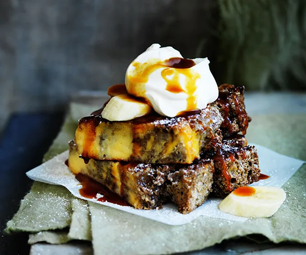 Banana bread French toast topped with whipped cream and banana slices, drizzled with syrup.