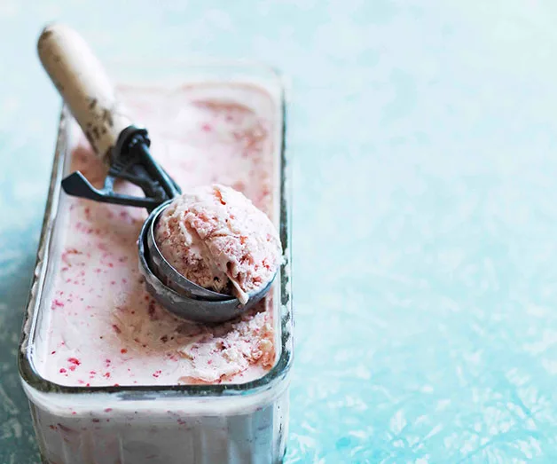 Rectangular container of strawberry ice cream with a scoop on top, set against a light blue textured background.