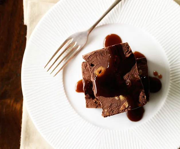Chocolate dessert with nuts and syrup on a white plate, with a fork beside it.