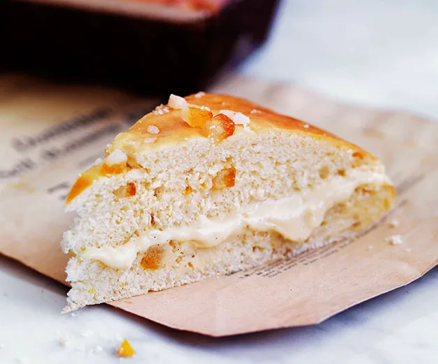 A slice of roscón de reyes filled with cream, garnished with candied fruit, placed on a piece of brown paper.