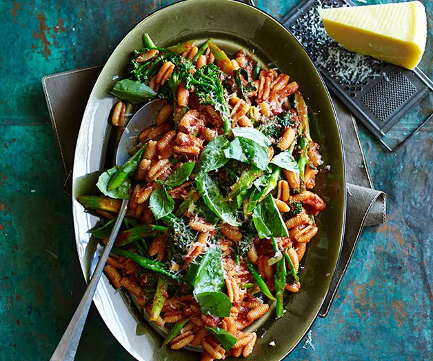 Plate of cavatelli pasta with tomato sauce, greens, and parmesan, with a wedge of cheese on the side.