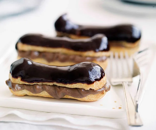 Chocolate eclairs topped with glossy dark chocolate glaze on a white plate with a fork.