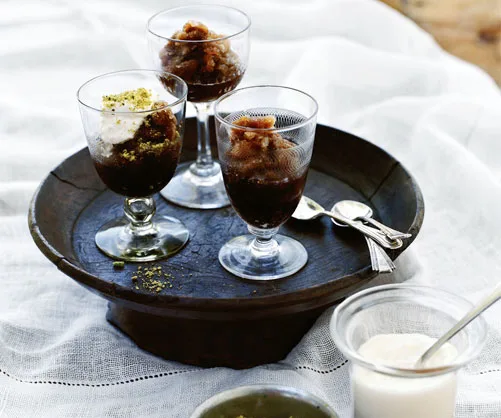Three glasses of coffee granita on a dark tray, topped with whipped cream and nuts, on a white tablecloth.