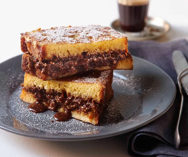 Grilled chocolate sandwiches dusted with powdered sugar on a gray plate, with a cup of espresso in the background.