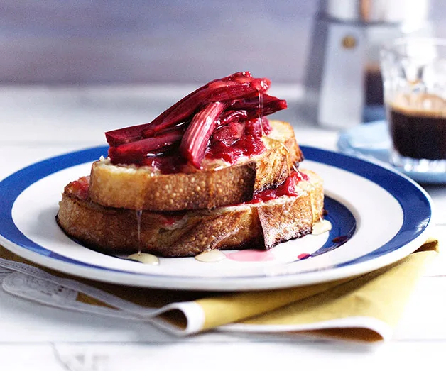 French toast topped with rhubarb and syrup on a blue-rimmed plate, next to a coffee cup.
