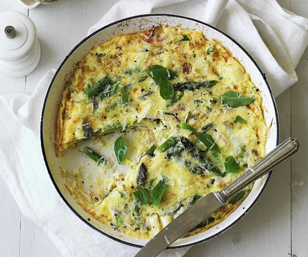 Frittata with asparagus and herbs in a pan on a white cloth, with a serving knife.