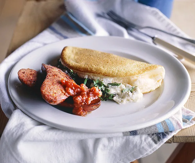 Omelet with greens and cheese on a plate, served with cooked sausage slices and tomato sauce.