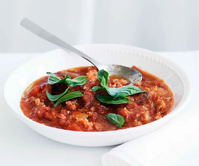 Bowl of tomato and bread soup garnished with fresh basil leaves, with a spoon resting inside the bowl.