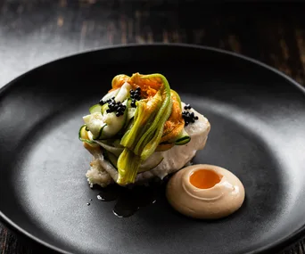Plate of gourmet food with zucchini flowers, caviar, and sauce on a black dish.