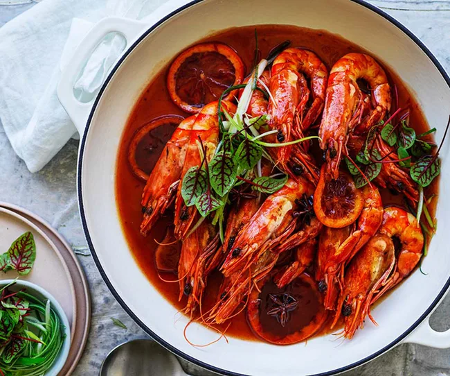 Red prawns in a white dish with citrus slices and garnished with herbs.