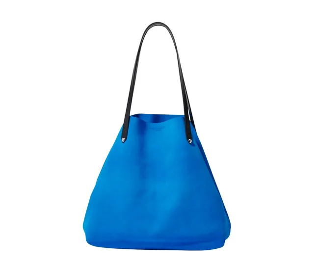 A blue tote bag with black leather handles on a white background.