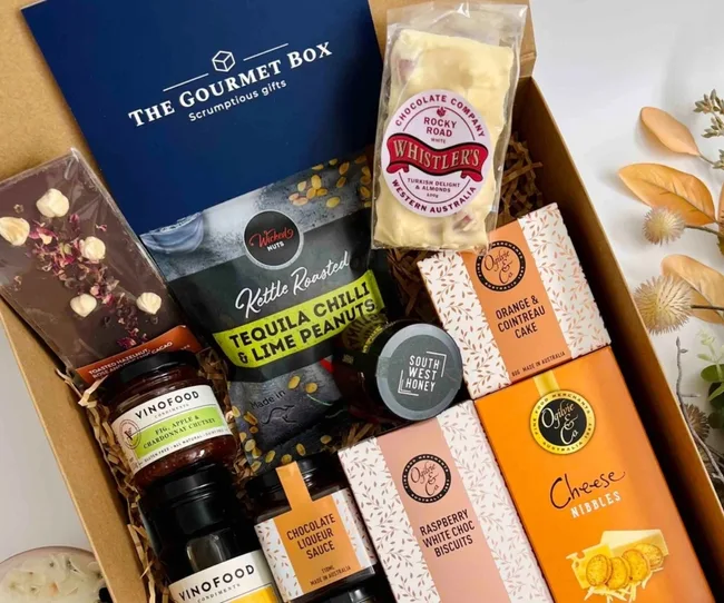 Gourmet gift box with assorted snacks, including chocolate, peanuts, chutney, cake, biscuits, and honey.