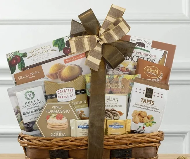 Gift basket with crackers, chocolates, and snacks, adorned with a large brown and gold bow.
