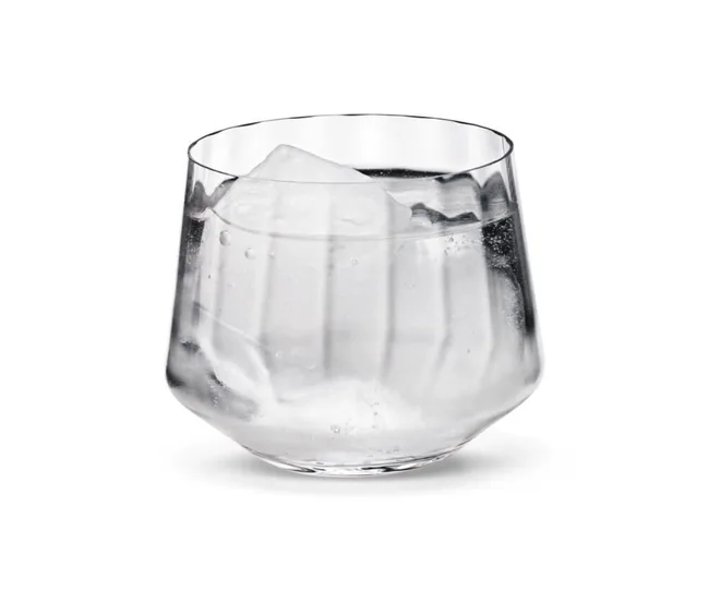 A faceted glass tumbler filled with water and a large ice cube on a white background.