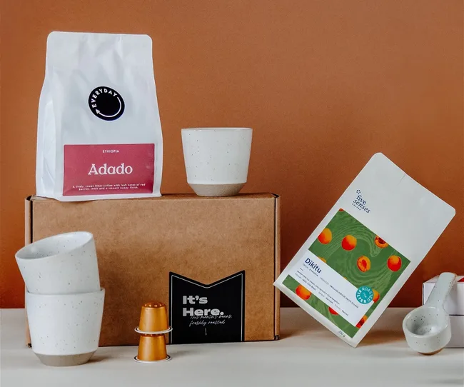 Coffee bags, cups, and capsules arranged on a box against a brown background.