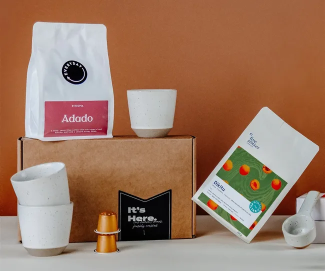 Coffee bags, cups, and capsules arranged on a box against a brown background.