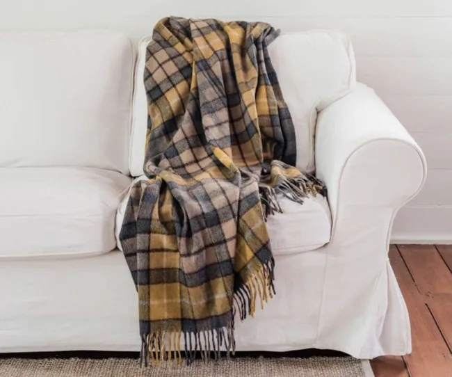 Plaid blanket in brown and gray tones draped over a white sofa inside a cozy room.