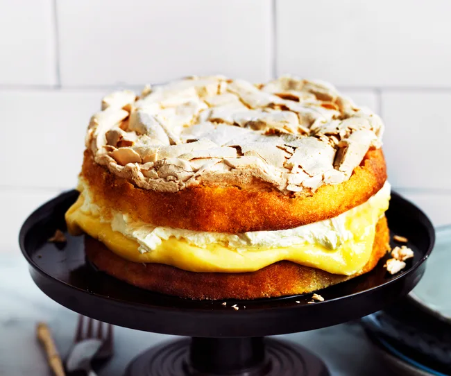Layered lemon cake with meringue topping and cream filling on a black cake stand.