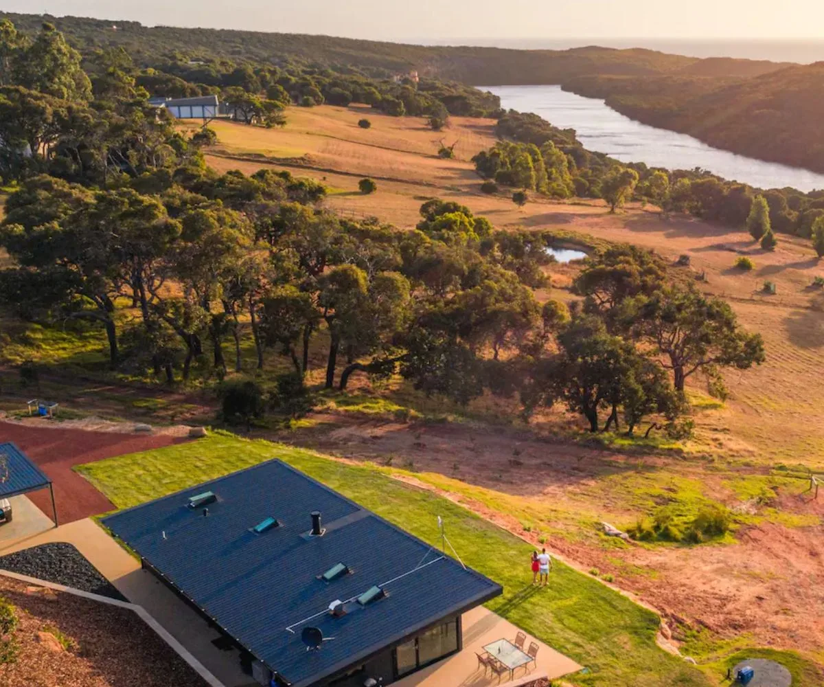 Aerial view of a rural landscape with a modern house, trees, and a river at sunset.