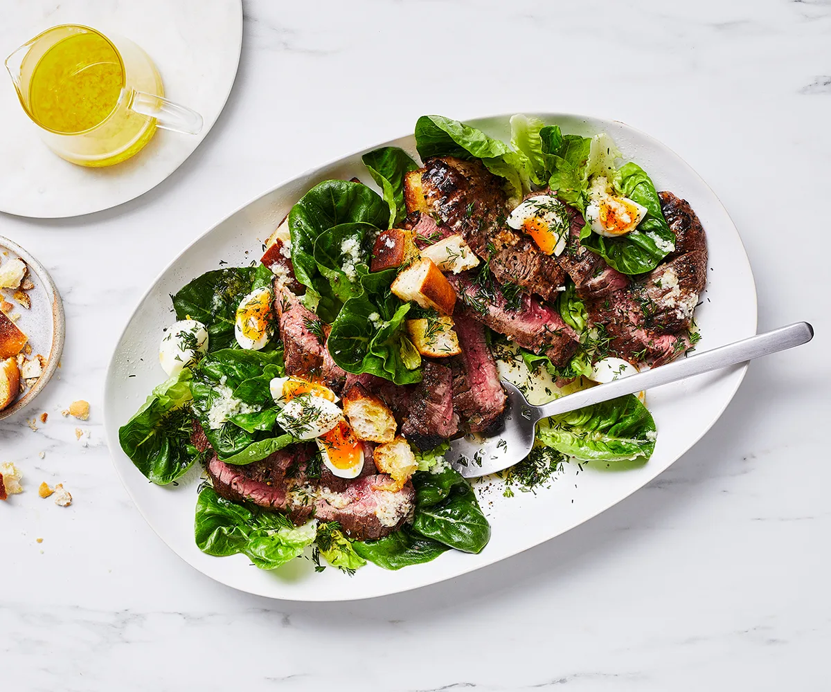 An aerial view of an oval platter filled with grilled chopped pepper steak with baby lettuce salad.