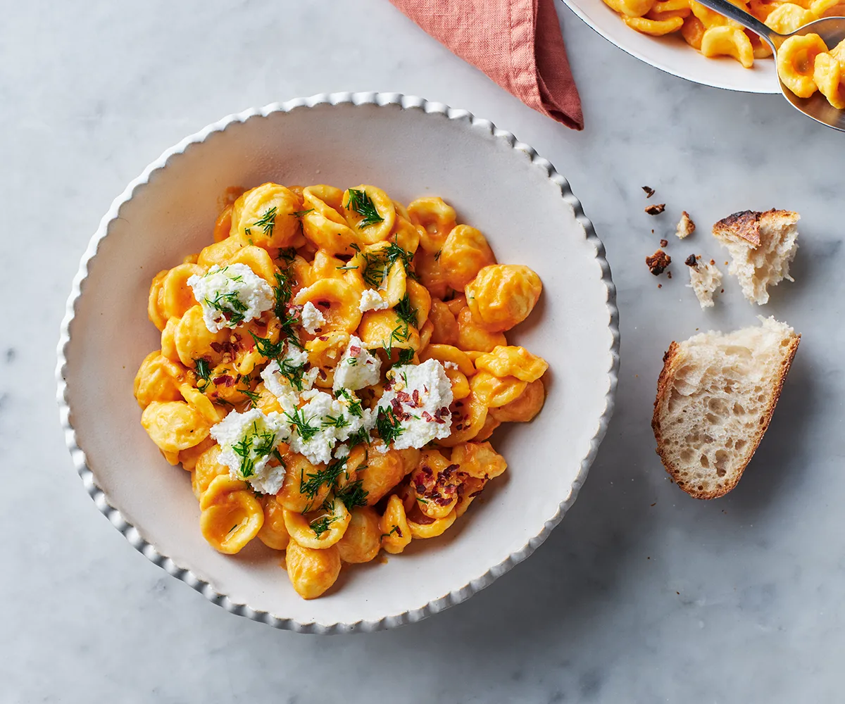 An aerial view of a bowl with ajvar orecchiette with crusty bread on the side.